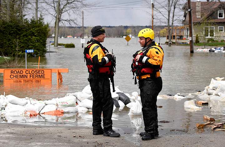 Ottawa Firefighters talk next to a flooded section of road at the Ottawa River in the neighbourhood of Cumberland, as rising river levels and heavy rains continue to cause flooding, on Sunday, May 7, 2017.