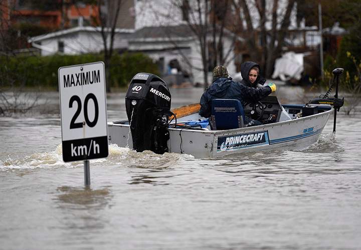 People in a motor boat pass a sign on Voisine Road in Rockland, Ont., about 40 kilometres east of Ottawa on Sunday, May 7, 2017.