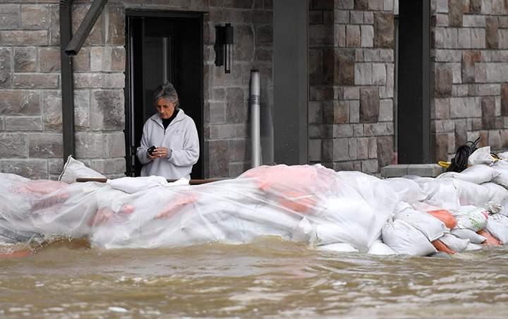 A resident uses her phone from behind sandbags at the front of a home on Voisine Road in Rockland, Ont., about 40 kilometres east of Ottawa, on Sunday, May 7, 2017.
