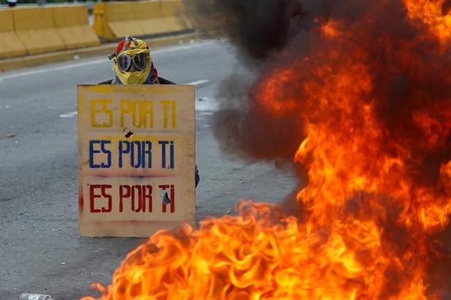 A demonstrator hols a sign that doubles a shield that reads in Spanish "It's for you," during a national sit-in against President Nicolas Maduro, in Caracas, Venezuela, Monday, May 15, 2017.