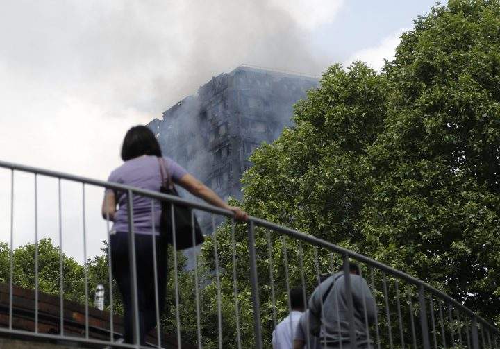 The high-rise apartment building where a massive fire raged smoulders as people cross a pedestrian bridge nearby, in London, June 14, 2017.