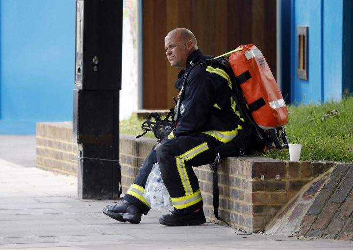 A fire officer rests near the high-rise apartment building where a massive fire raged overnight in London.