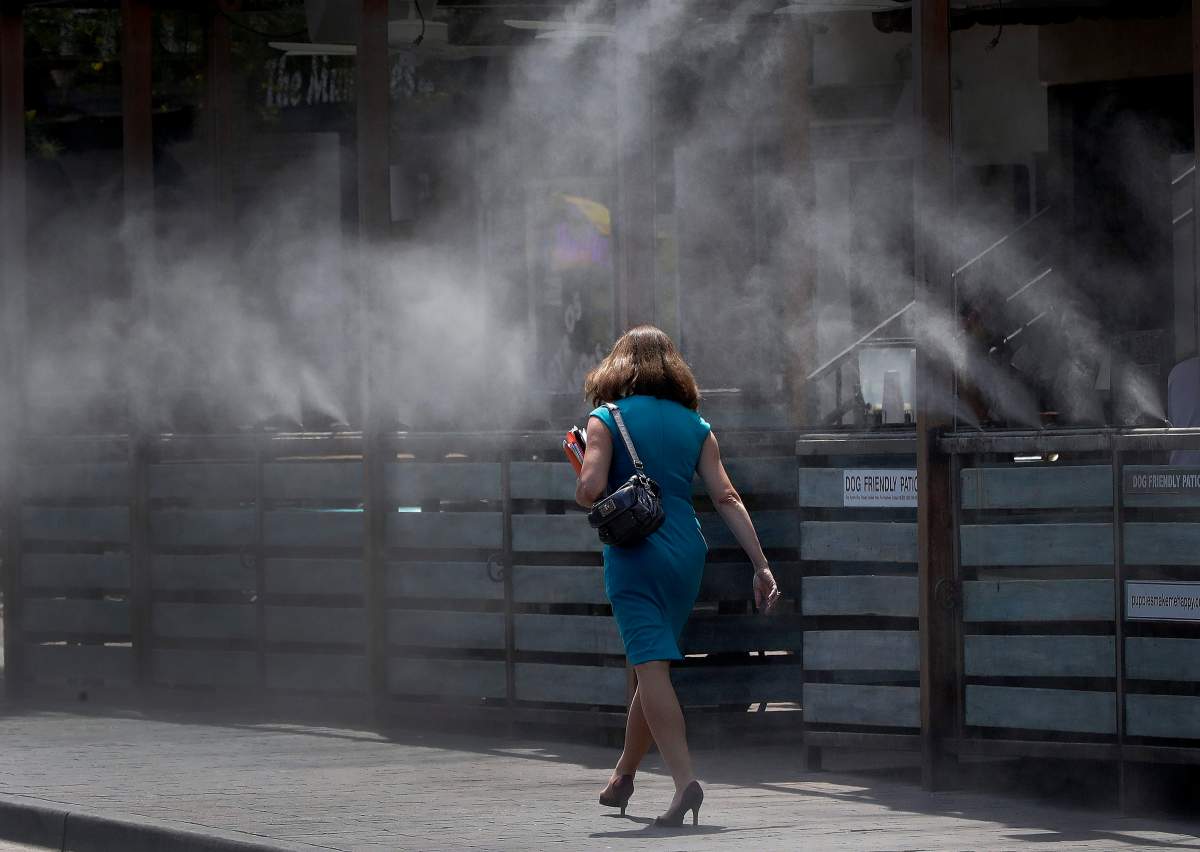 A woman walks along a row of misters Monday, June 19, 2017 in Tempe, Ariz. The forecast calls for a high of 118 on Monday and 120 on Tuesday in Phoenix.