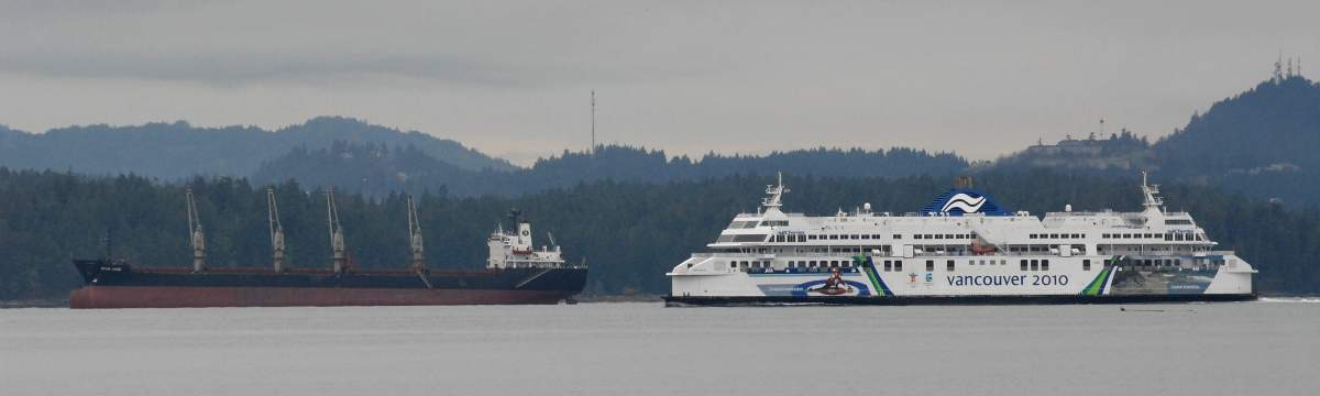The BC Ferries' vessel Coastal Inspiration passes a freighter anchored off Vancouver Island as it heads for the terminal at Nanaimo, BC, Canada. The ferry was coming from Horseshoe Bay on the British Columbia mainland. 