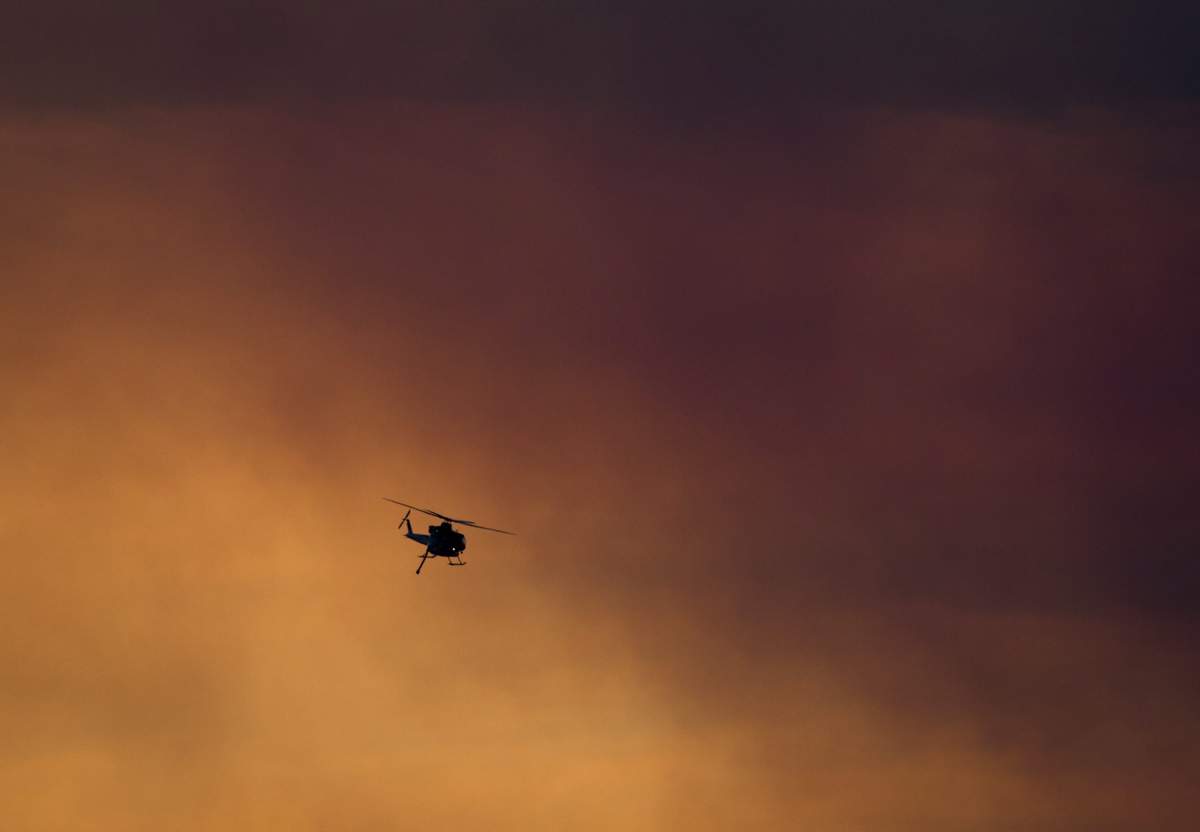 A firefighting helicopter flies past smoke in the air from a wildfire burning near Ashcroft, B.C., at sunset on Friday July 7, 2017.