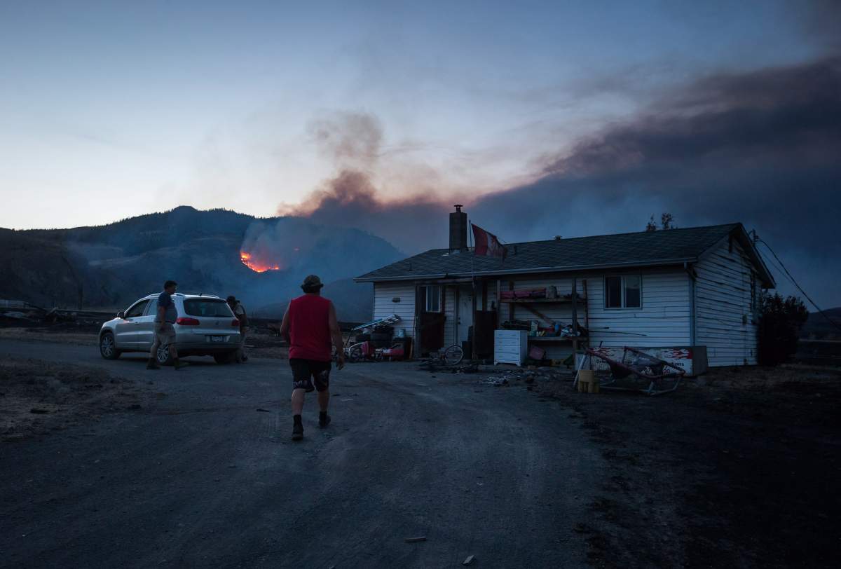 Darin Minnabarriet walks to his house that survived a wildfire to empty his freezer on the Ashcroft First Nation, as a fire burns on a mountain in the distance near Ashcroft, B.C., late Sunday July 9, 2017. THE CANADIAN PRESS/Darryl Dyck