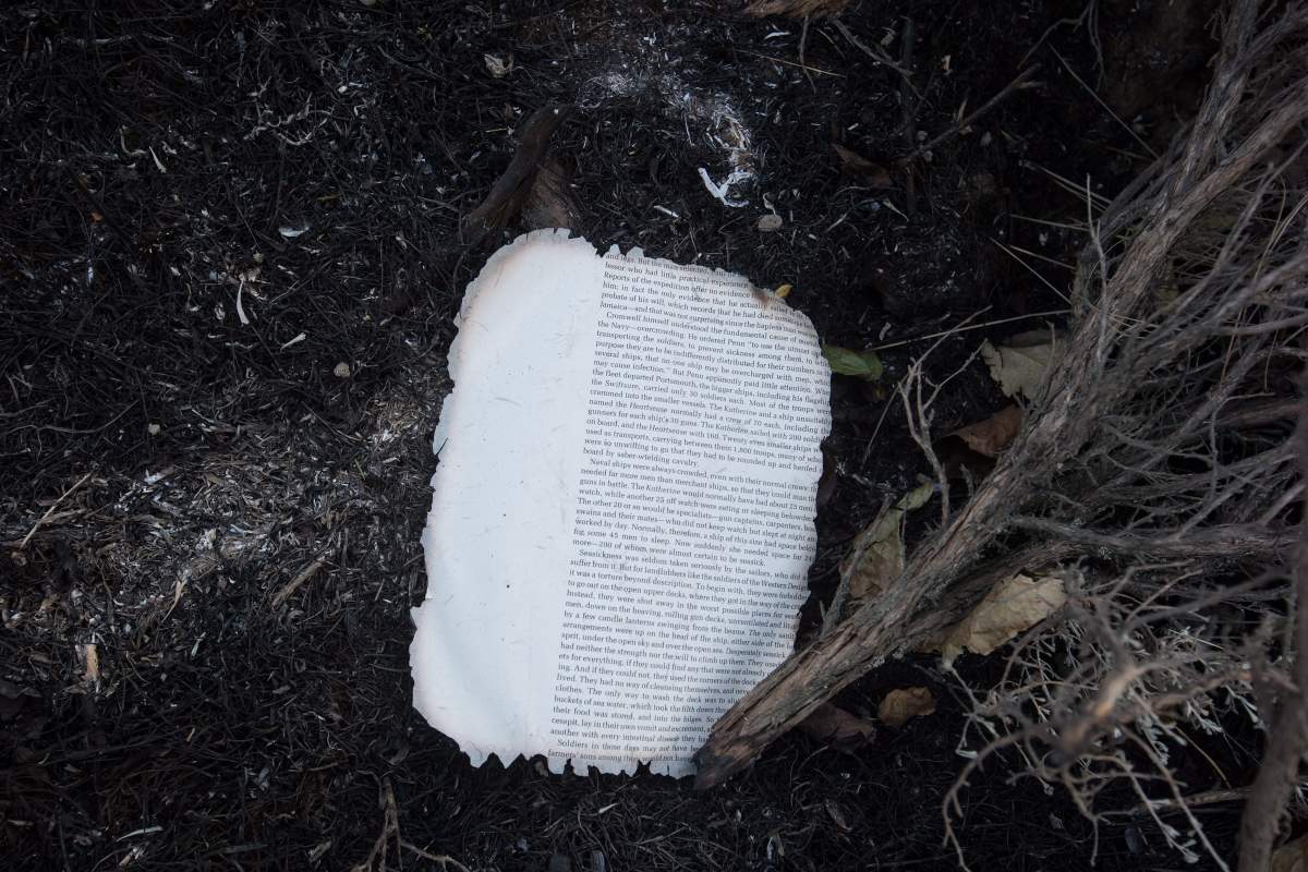 A burnt page from a book is seen on the ground near the remains of mobile homes destroyed by wildfire in Boston Flats, B.C., on Sunday July 9, 2017. B.C. government officials now estimate that 7,000 people have been evacuated from their homes due to wildfires burning in the province. THE CANADIAN PRESS/Darryl Dyck