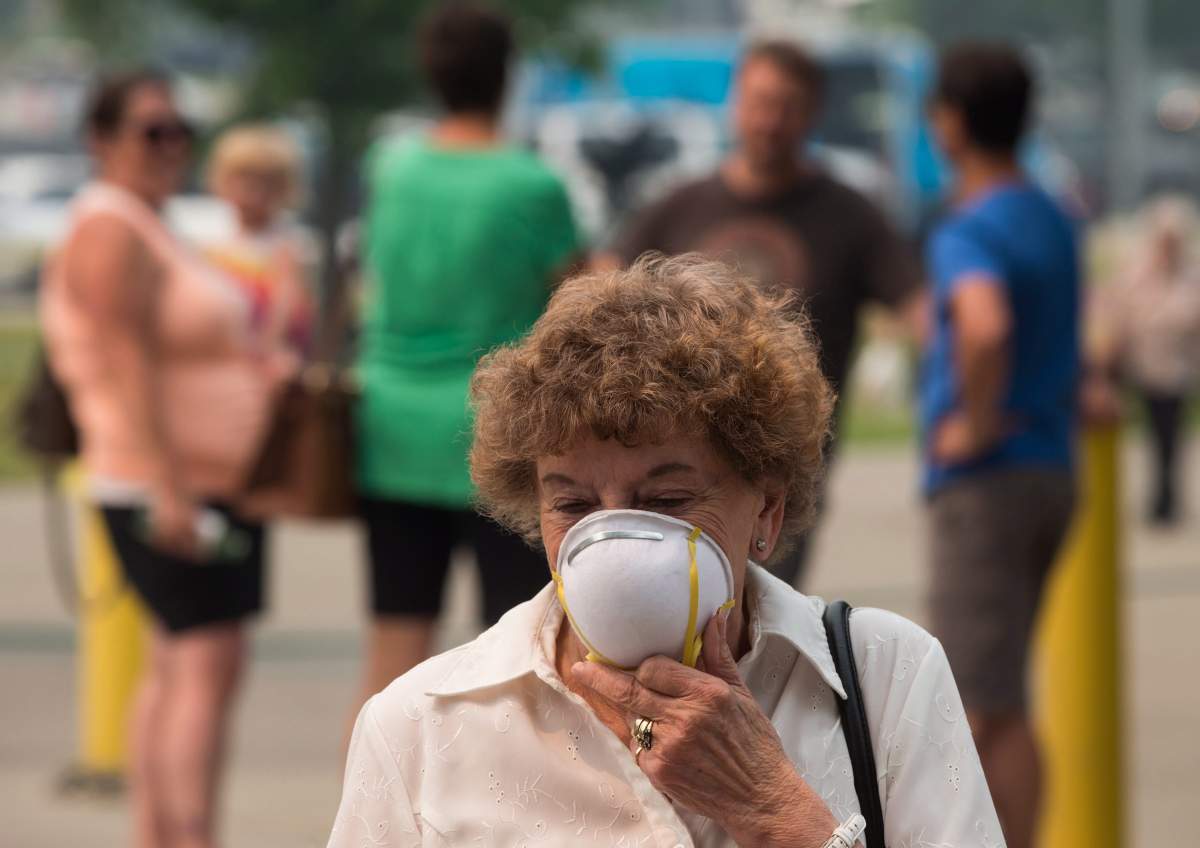 Marina Stephenson, 78, who was evacuated from Cache Creek due to a wildfire holds a particle mask to her face because of smoke in the air, outside an evacuation registration centre in Kamloops, B.C., on Monday July 10, 2017. More than 200 wildfires are burning in the province and an estimated 14,000 people have been evacuated from their homes. THE CANADIAN PRESS/Darryl Dyck