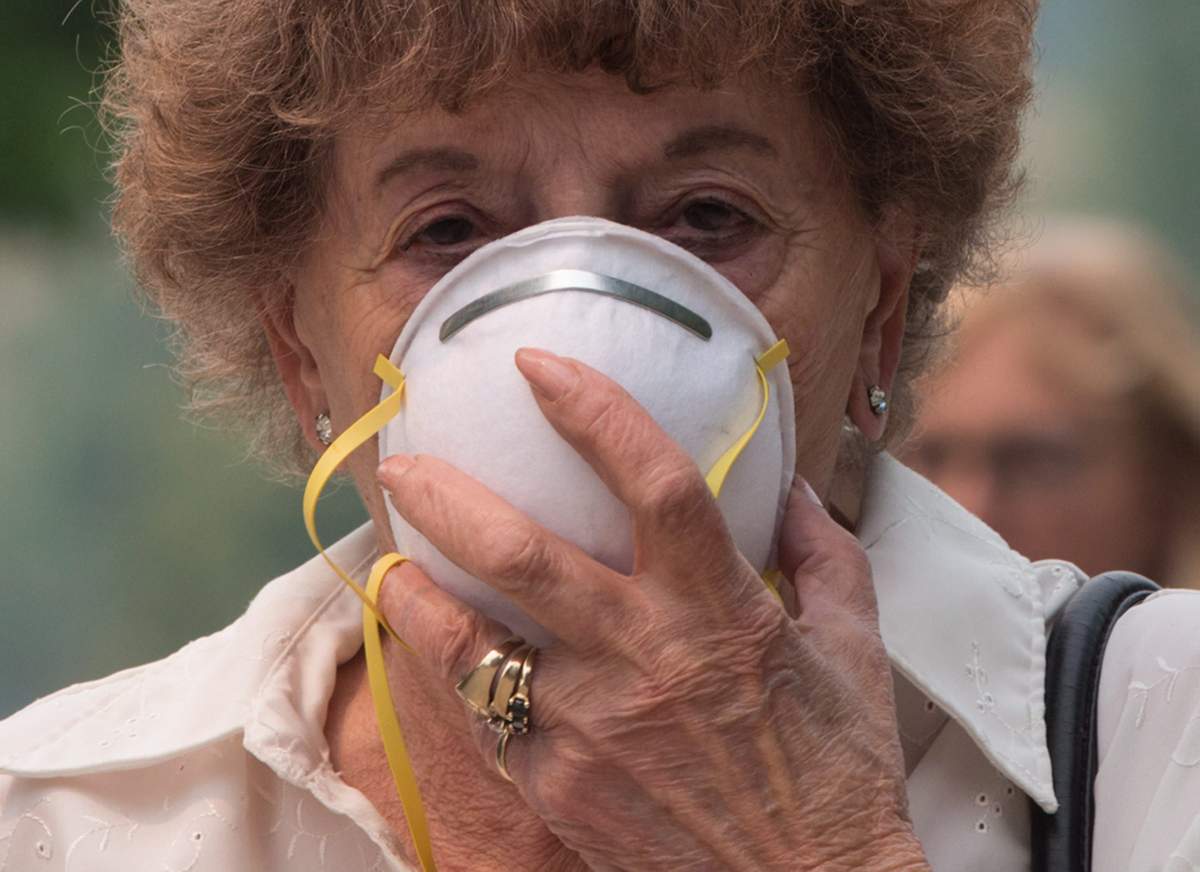 Marina Stephenson, 78, who was evacuated from Cache Creek due to a wildfire, holds a particle mask to her face because of smoke in the air, outside an evacuation registration centre in Kamloops, B.C., on Monday July 10, 2017. More than 200 wildfires are burning in the province and an estimated 14,000 people have been evacuated from their homes. THE CANADIAN PRESS/Darryl Dyck