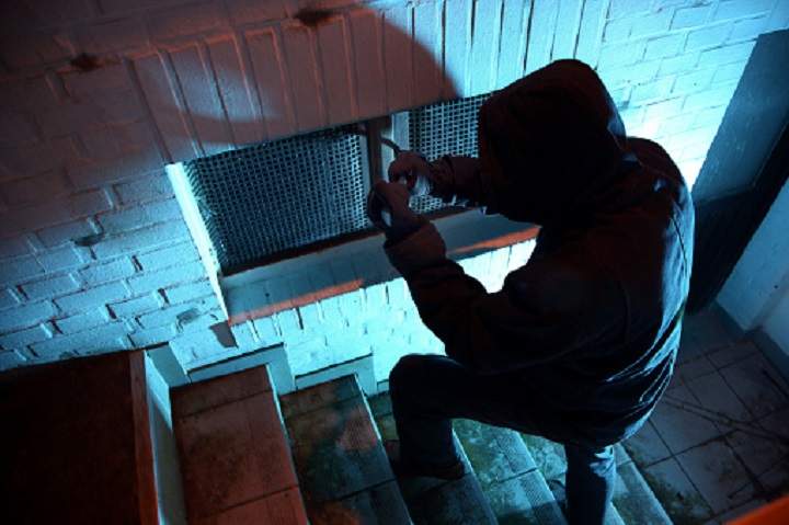 FILE PHOTO: A burglar breaking into a basement window.