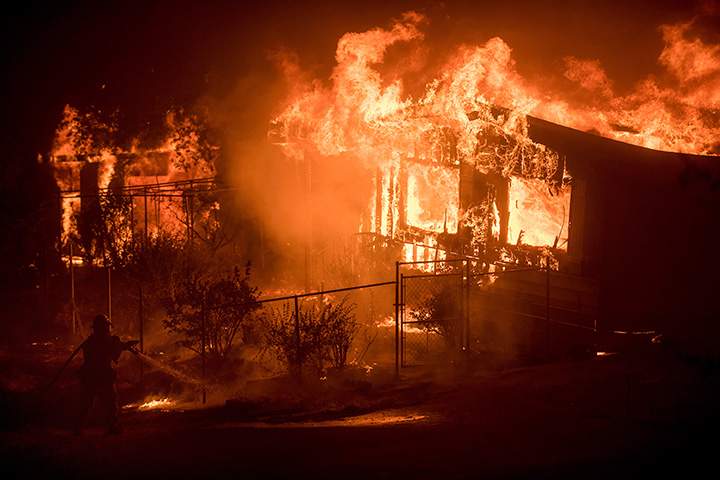 A firefighter sprays water as flames from consume a residence near Oroville, Calif., on Sunday, July 9, 2017.