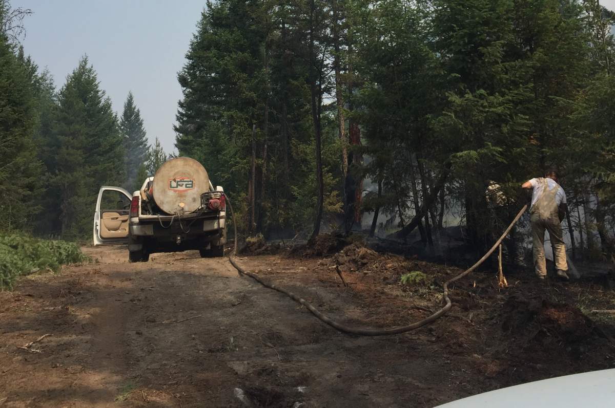 Ranchers use a water tank in the back of a pickup to try and hose down dry brush.