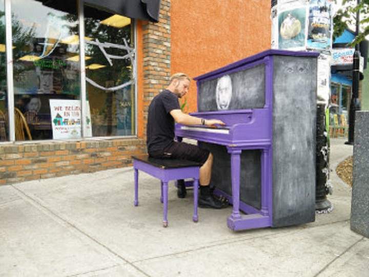 A man plays a piano in front of The Carrot Community Arts Coffeehouse. The purple one was replaced with a white one after three years of use.