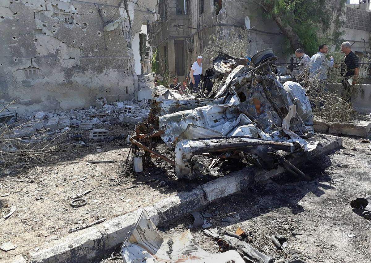 This photo released by the Syrian official news agency SANA, shows people gathering at the scene of an explosion along the road to the airport in southeast Damascus, Syria, Sunday, July 2, 2017.