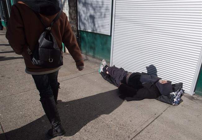 A woman walks past a man sleeping on the street in the Downtown Eastside of Vancouver, B.C., on Tuesday, February 21, 2017.