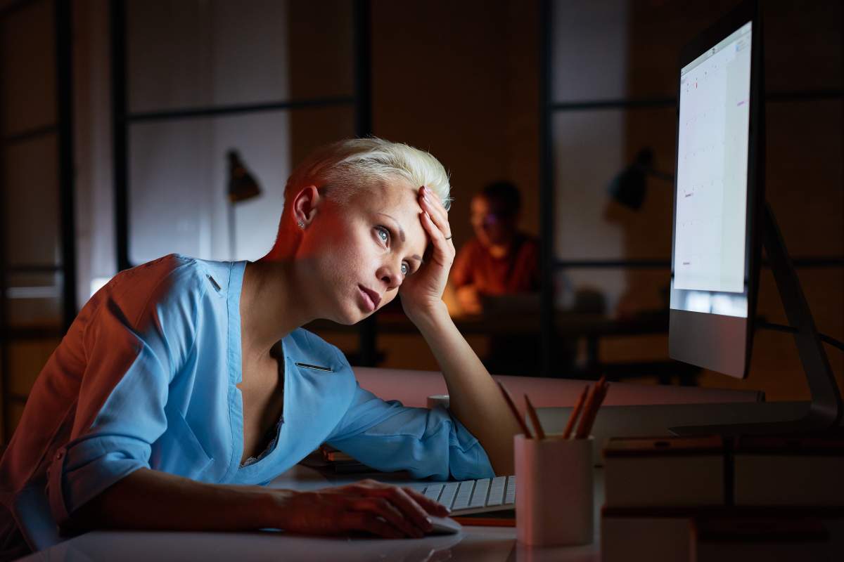 Tired puzzled businesswoman looking with disappointment at computer monitor and leaning on hand at table.