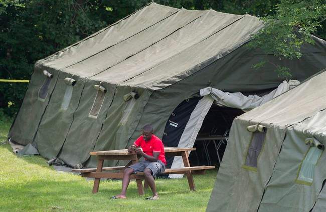 An asylum seeker checks his phone next to a tent at the Canada-United States border in Lacolle, Que. Thursday, August 10, 2017.