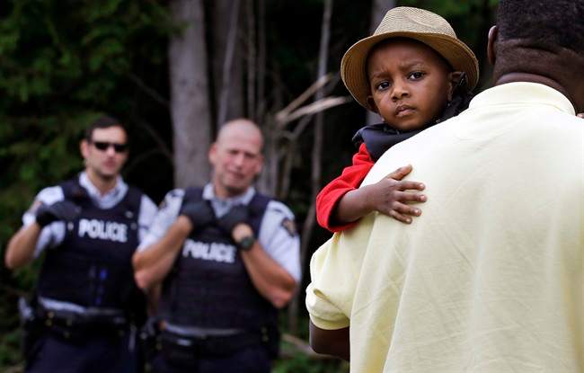 A Haitian boy holds onto his father as they approach an illegally crossing point, staffed by Royal Canadian Mounted Police officers, from Champlain, N.Y., to Saint-Bernard-de-Lacolle, Quebec, Monday, Aug. 7, 2017. Seven days a week, 24-hours a day people from across the globe are arriving at the end of a New York backroad so they can walk across a ditch into Canada knowing they will be instantly arrested, but with the hope the Canadian government will be kinder to them than the United States.