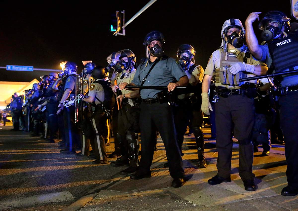 In this photo taken Aug. 18, 2014, police is riot gear work to disperse a crowd of protesters in Ferguson, Mo. 