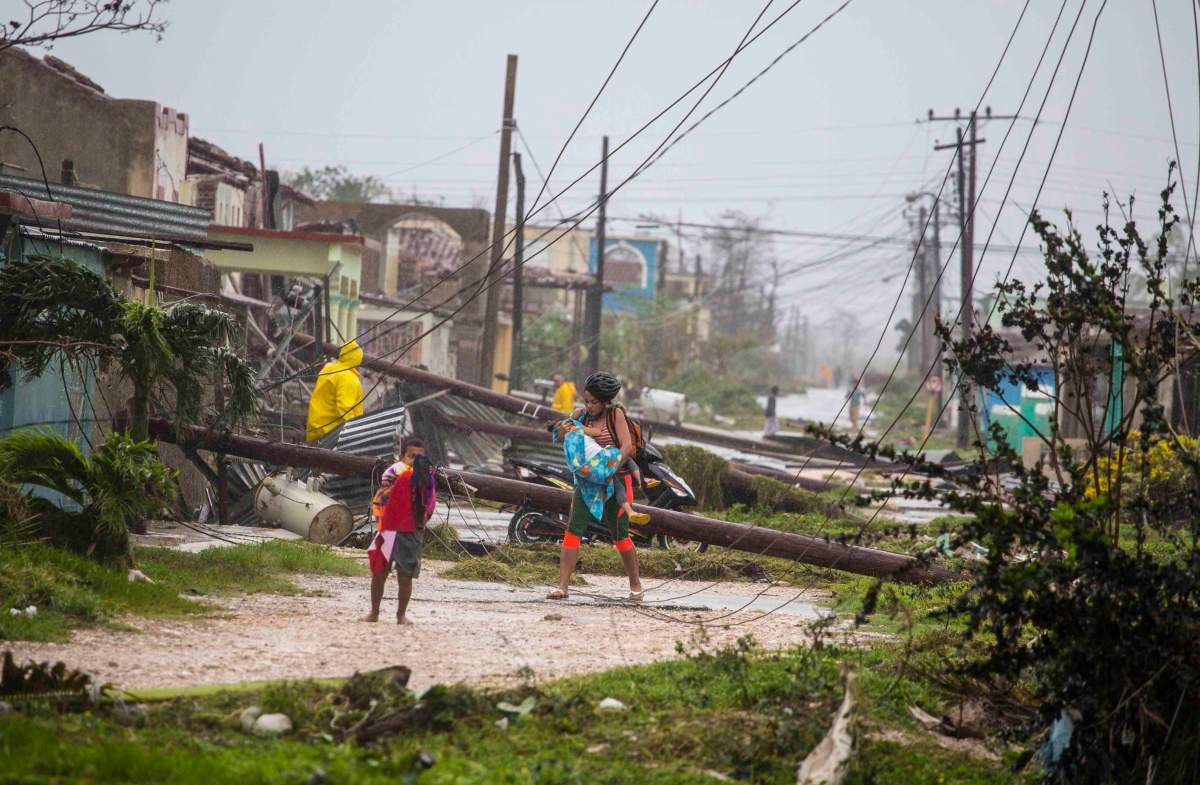 Residents walk near downed power lines felled by Hurricane Irma, in Caibarien, Cuba, Saturday, Sept. 9, 2017.