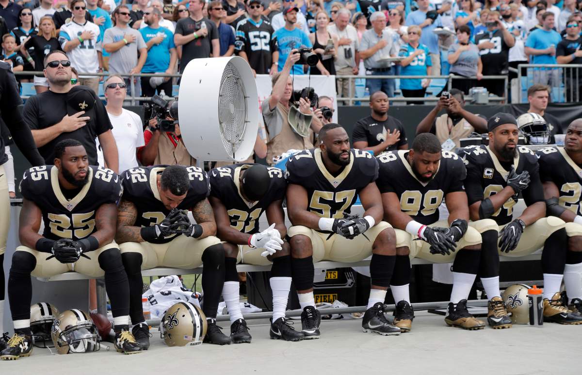 Saints players sit during the anthem