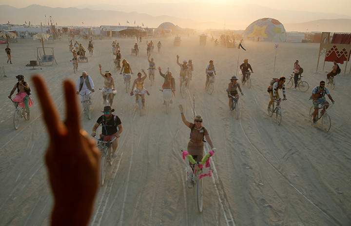 Burning Man participants react as a person on an art car waves and flashes them a peace sign as they bicycle through Black Rock City during the 4th day of the annual arts and music festival in Nevada, August 31, 2017.