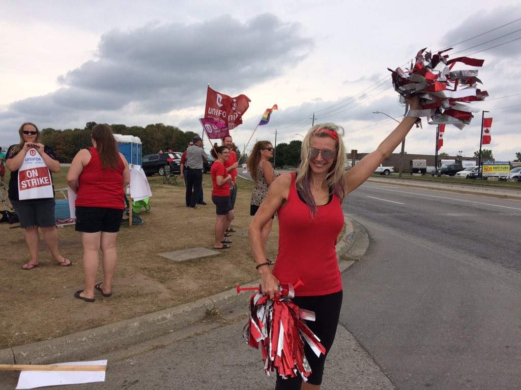 Denise Harrison waves pom poms, as drivers passing by lay on their horns in a show of support.
