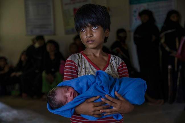 Rohingya Muslim girl Afeefa Bebi, who recently crossed over from Myanmar into Bangladesh, holds her few-hours-old brother as doctors check her mother Yasmeen Ara at a community hospital in Kutupalong refugee camp, Bangladesh, Wednesday, Sept. 13, 2017. The family crossed into Bangladesh on Sept. 3.
