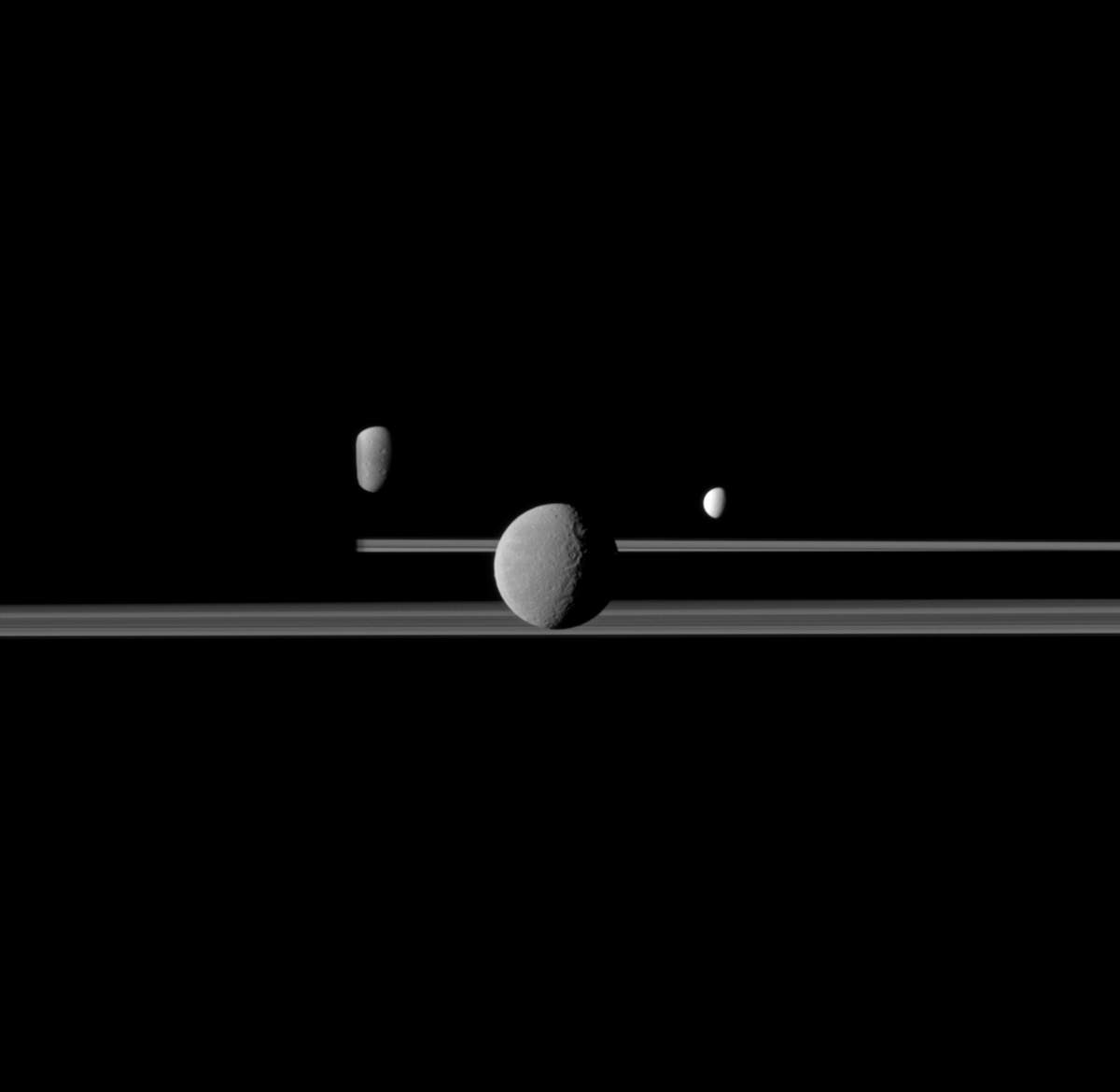 The Cassini spacecraft observes three of Saturn's moons set against the darkened night side of the planet. Rhea, Enceladus and Dione. 
