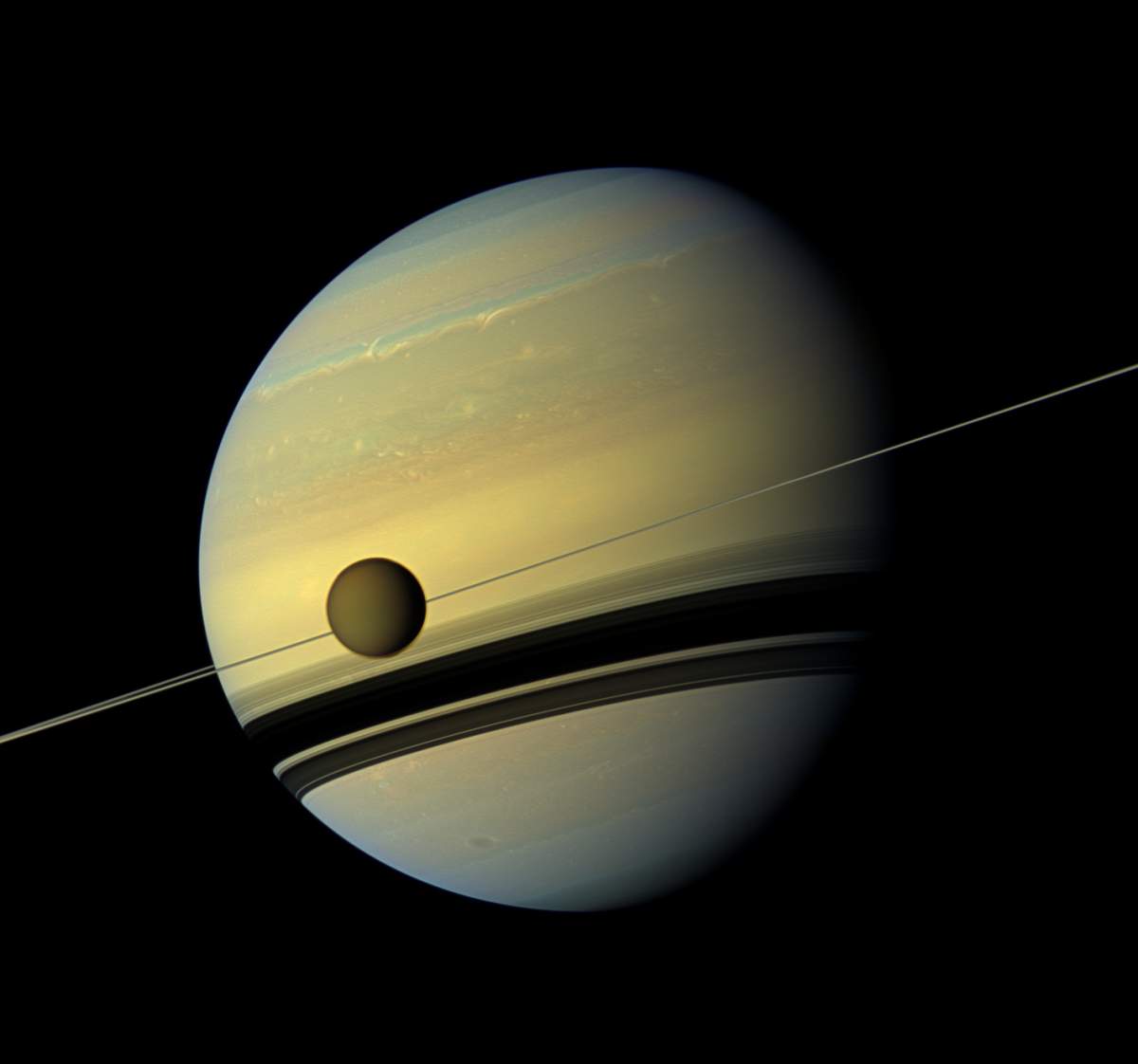 A giant of a moon appears before a giant of a planet undergoing seasonal changes in this natural color view of Titan and Saturn from NASA’s Cassini spacecraft.