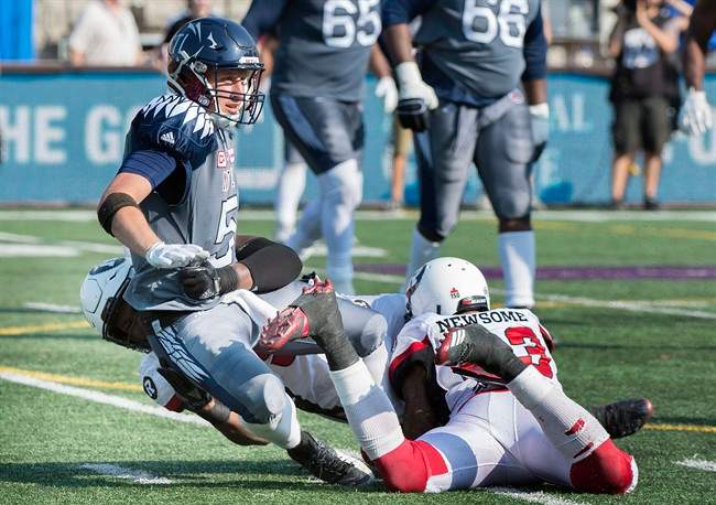 Montreal Alouettes quarterback Drew Willy, centre, is pulled down by Ottawa Redblacks' Avery Ellis, left, and Jonathan Newsome during second half CFL football action in Montreal, Sunday, September 17, 2017.