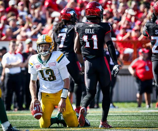 Edmonton Eskimos' quarterback Mike Reilly, left, picks himself up after being sacked by Calgary Stampeders' Junior Turner, centre, and teammate Josh Bell during second half CFL football action in Calgary, Monday, Sept. 4, 2017.