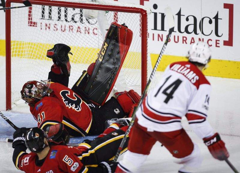 Carolina Hurricanes' Justin Williams, right, scores as Calgary Flames goalie Mike Smith, centre, and Mark Giordano try to block the net during third period NHL hockey action in Calgary, Thursday, Oct. 19, 2017.