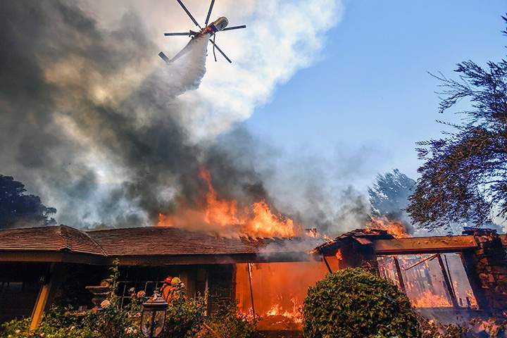 A helicopter dumps water on a home as firefighters battle a wildfire in Anaheim Hills, California, Monday, Oct. 9, 2017.