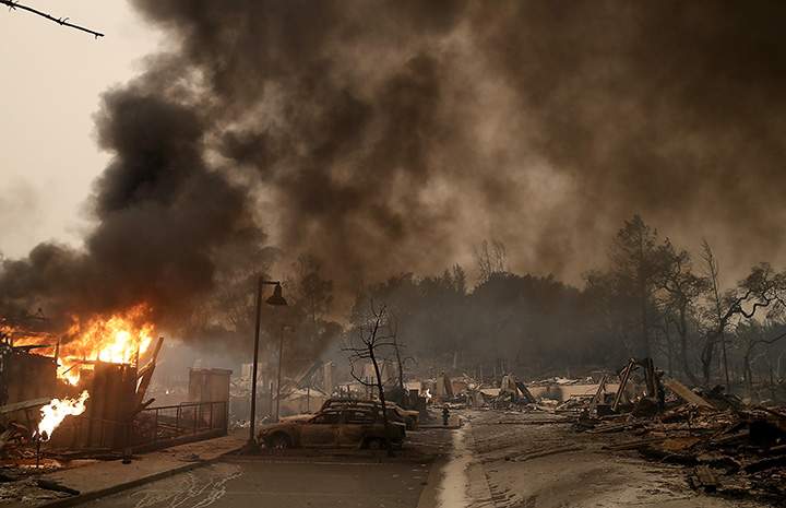 Burned out cars sit next to a building on fire in Santa Rosa, California on October 9, 2017.