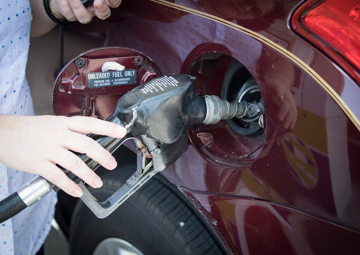 Woman's hand holding a pump nozzle in car fuel tank door.