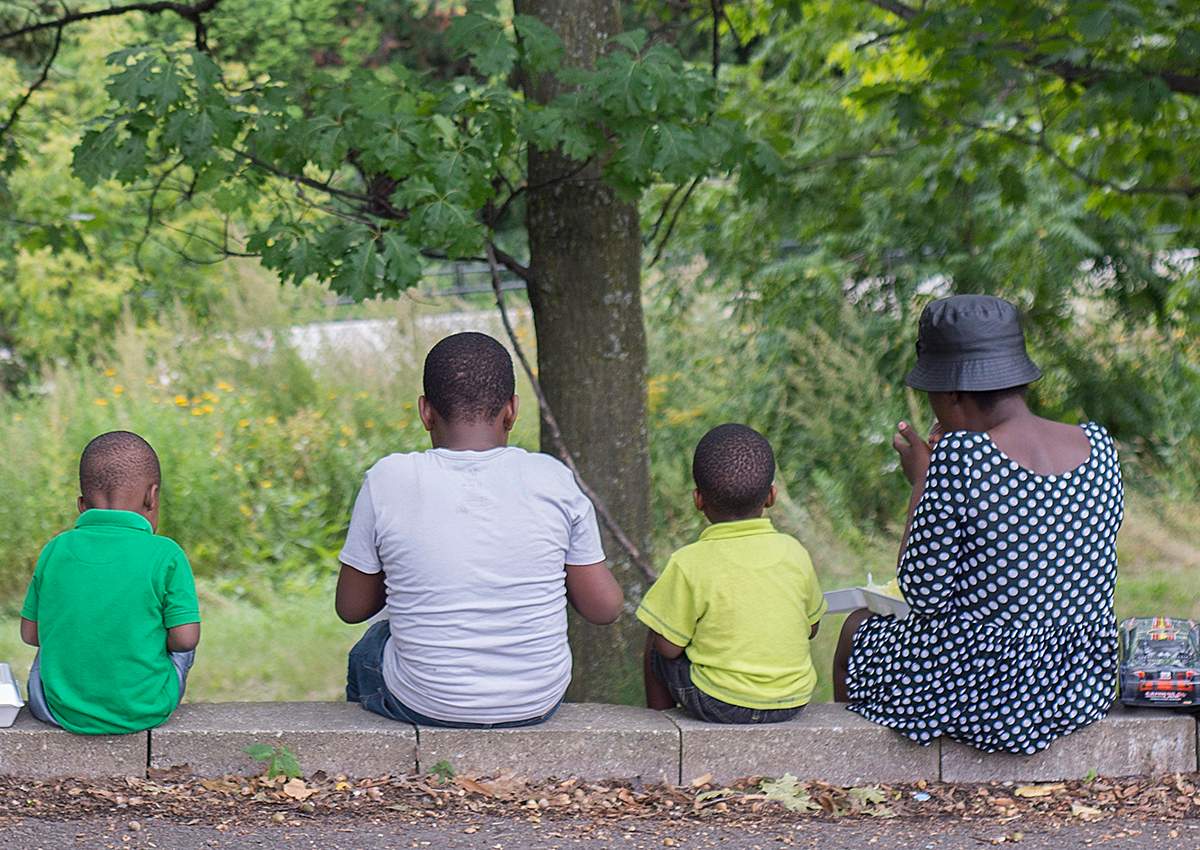 Women and children eat food handed out by a local Haitian church in a park next to the Olympic Stadium in Montreal on Thursday, August 31, 2017. 