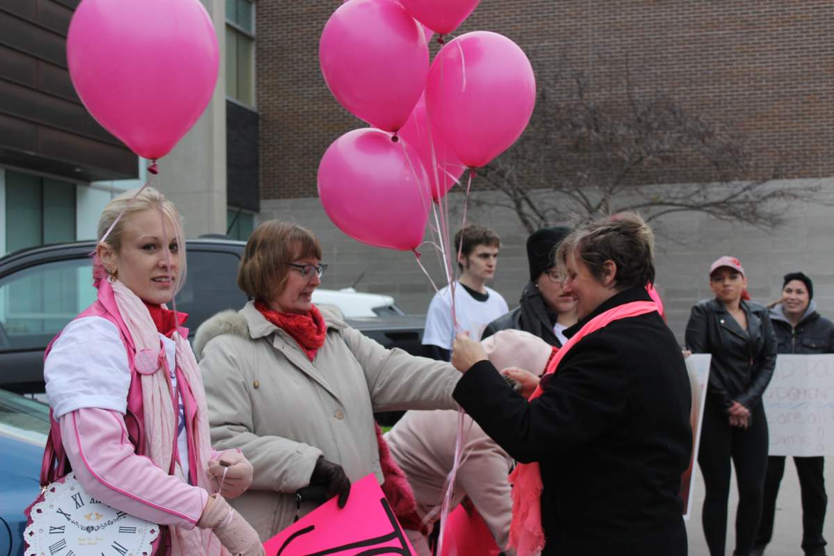 Fanshawe College School of Nursing professor Jodi Hall hands out balloons to march participants, outside of police headquarters.