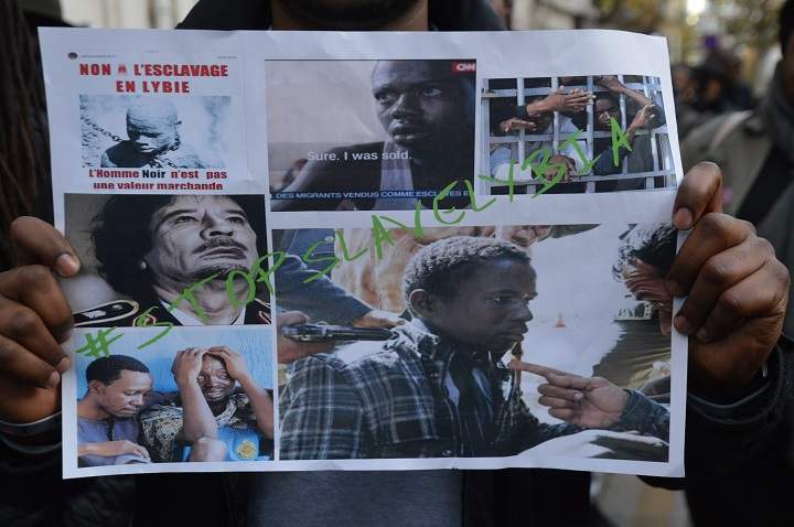 A man holds a sign depicting migrants in Libya reading ‘Stop slavery in Libya’ during a march against slavery in Libya on November 18, 2017 in Paris.