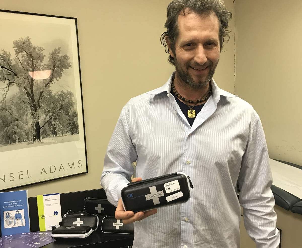 Neil Henderson, clinical psychotherapist – standing in front of a display of naloxone kits.