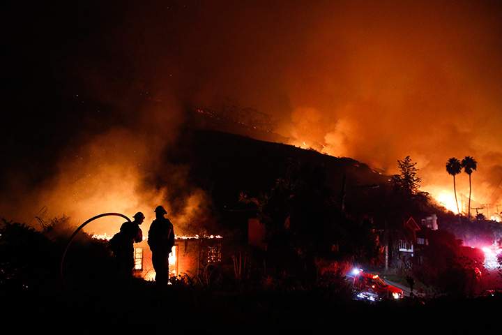 Two firefighters watch as a home burns in a wildfire in La Conchita, Calif. on Thursday, Dec. 7, 2017.