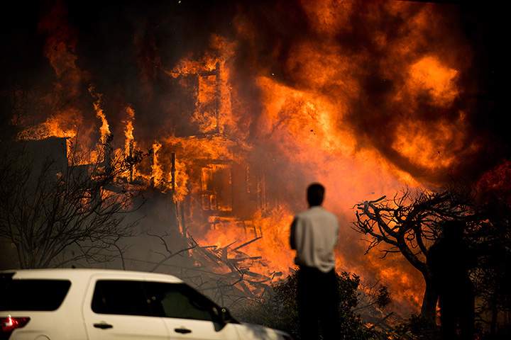 A man watches flames consume a residence as a wildfire rages in Ventura, Calif., Tuesday, Dec. 5, 2017.