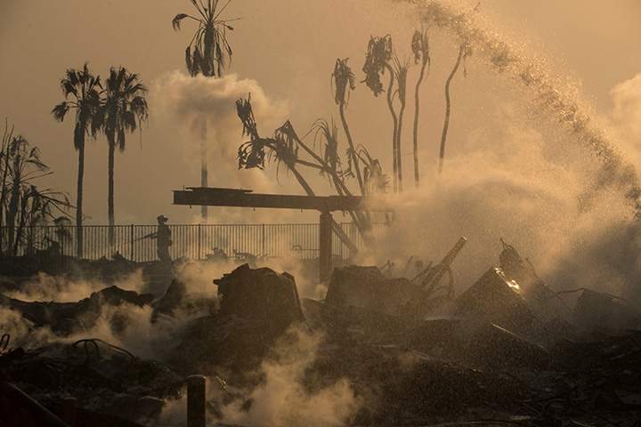 A firefighter sprays water on the remains of the Hawaiian Village apartments after a wind-driven wildfire swept into the city of Ventura, California, December 5, 2017.