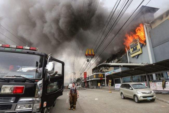 This photo taken on December 23, 2017 shows a firefighter standing in front of a burning shopping mall in Davao City on the southern Philippine island of Mindanao.