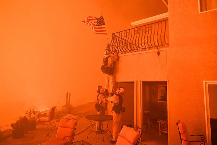 Firefighters remove a U.S. flag as flames from a wildfire close in on a luxury home in Oroville, California on July 8, 2017.