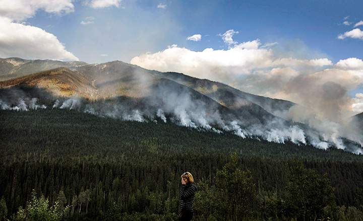 A woman stops on the side of the highway to watch a forest fire burn near Revelstoke B.C. on August 19, 2017.