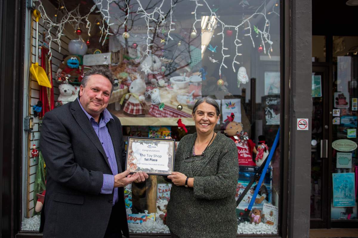 Peterborough DBIA Executive Director Terry Guiel presents Toy Shop owner Jean Grant with her first-place prize in the annual Holiday Window Contest.
