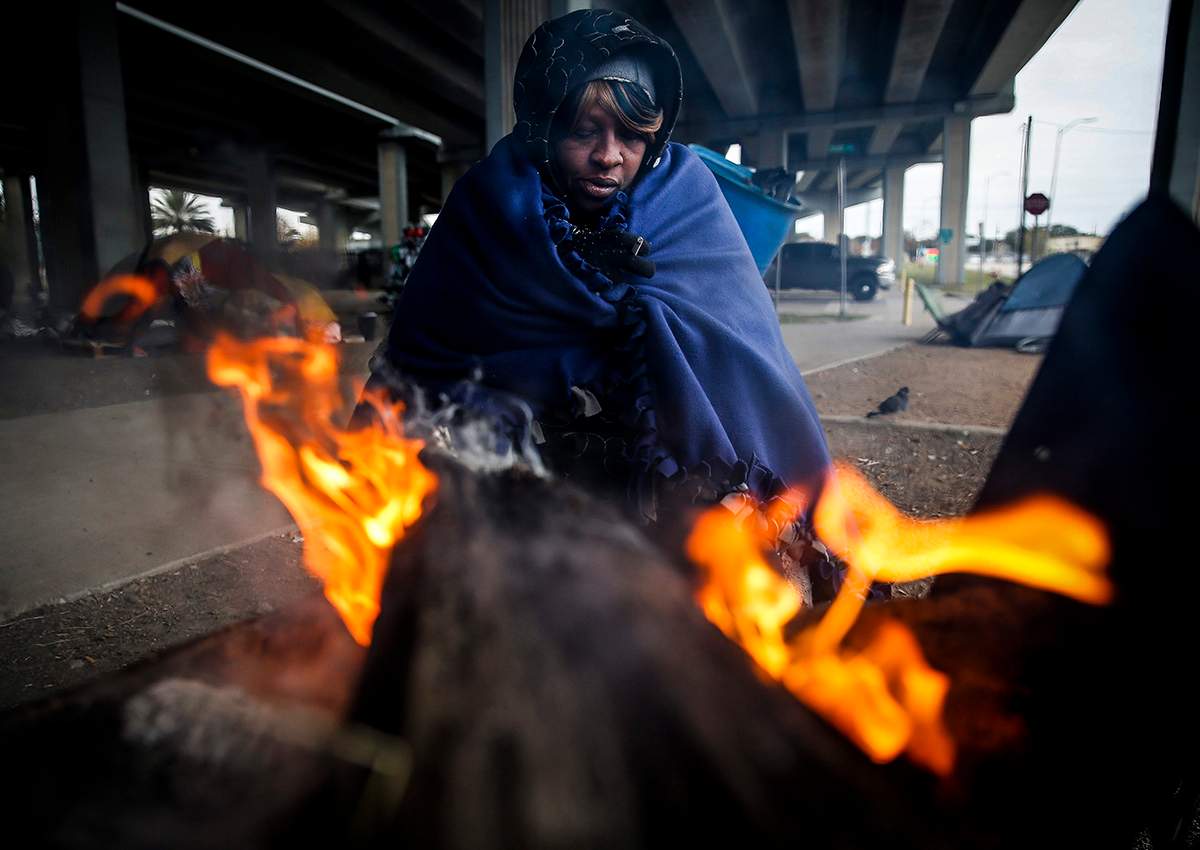 Tony Sampson, who received a blanket from Star of Hope’s Love in Action van, tries to warm up by a fire under the Eastex Freeway as temperatures hover in the 30s Tuesday, Jan. 2, 2018, in Houston.