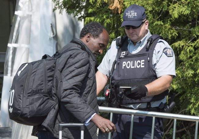 An asylum seeker shows his passport to an RCMP officer as crosses the border into Canada from the United States, Aug. 21, 2017 near Champlain, N.Y. 