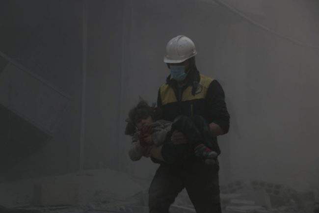 A Syrian civil defense team member carries a baby rescued from a wreckage after Assad regime forces carried out airstrikes over the de-escalation zone in Arbin town of Eastern Ghouta in Damascus, Syria on February 23, 2018.